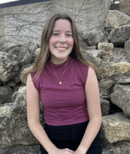A woman smiling in front of a stone wall. 